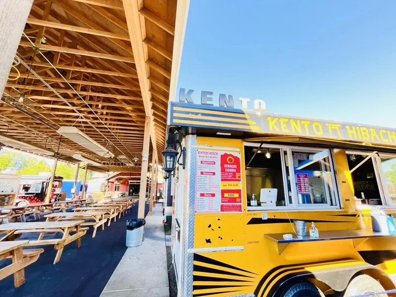 The yellow Kentochi Hibachi trailer with blue awning stripes under the timber roof of The Barn, picnic tables beside it